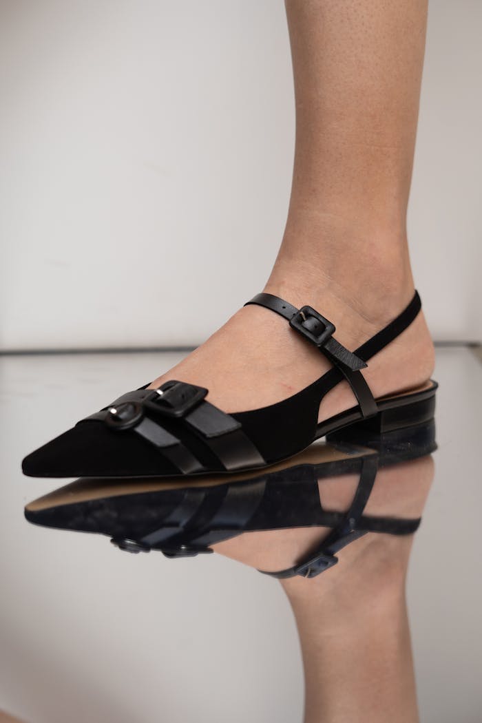 Close-up of a black suede slingback shoe with buckles, reflecting on a glossy surface. Fashion footwear style.
