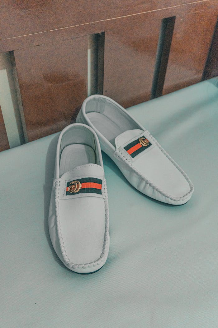 Close-up of stylish white leather loafers featuring a designer logo on a bed.